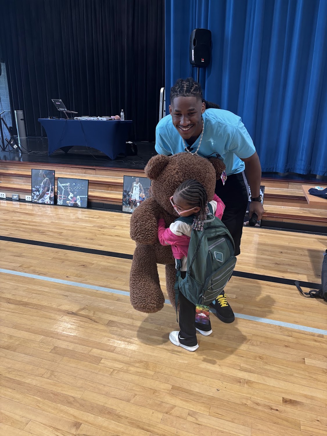 Silas Demary Jr. hugs a child holding a large teddy bear and backpack at the 2026 Raleigh Back to School Bash.