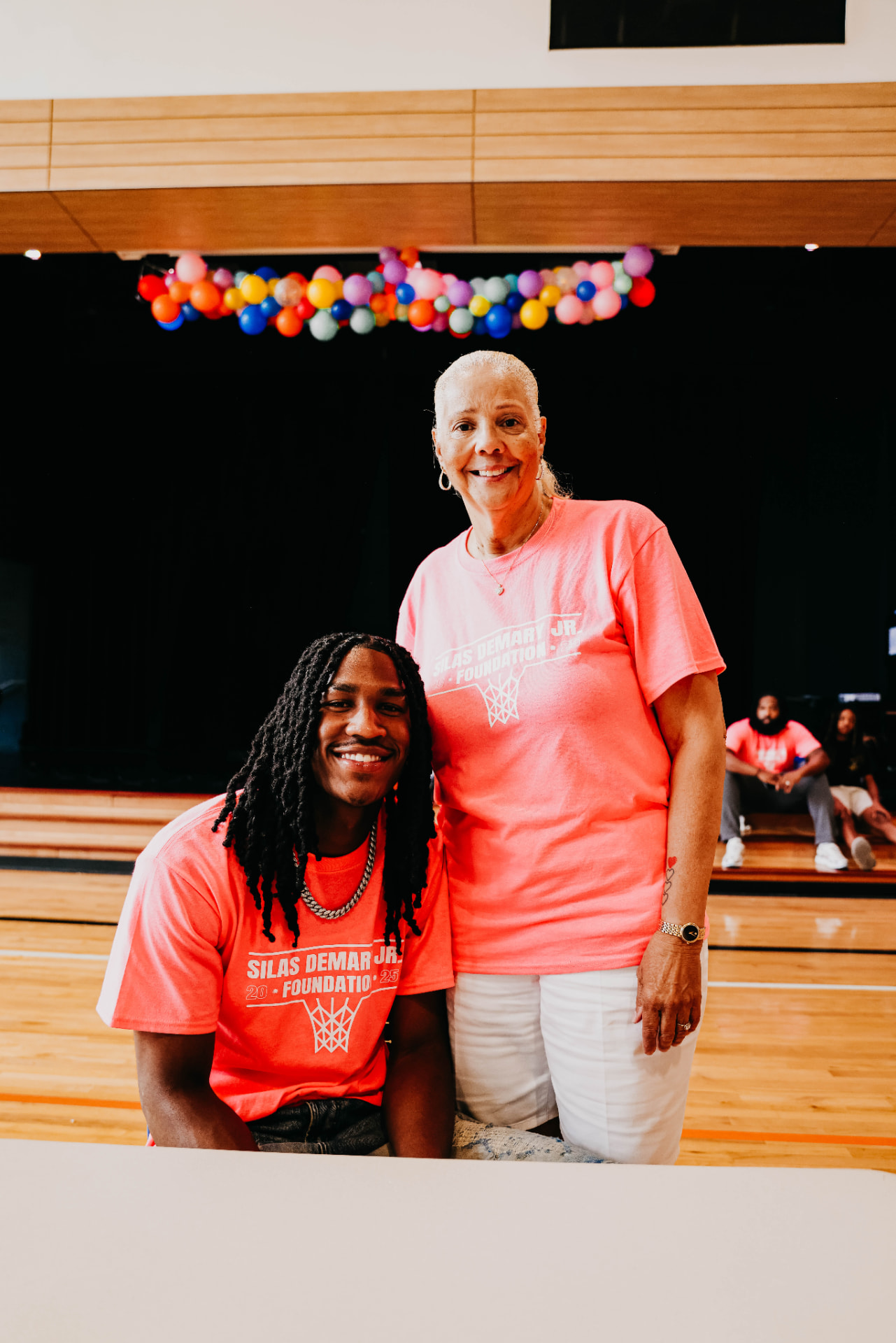 Silas Demary Jr. kneels beside a supporter in matching foundation shirts at the 2025 Back to School Bash.