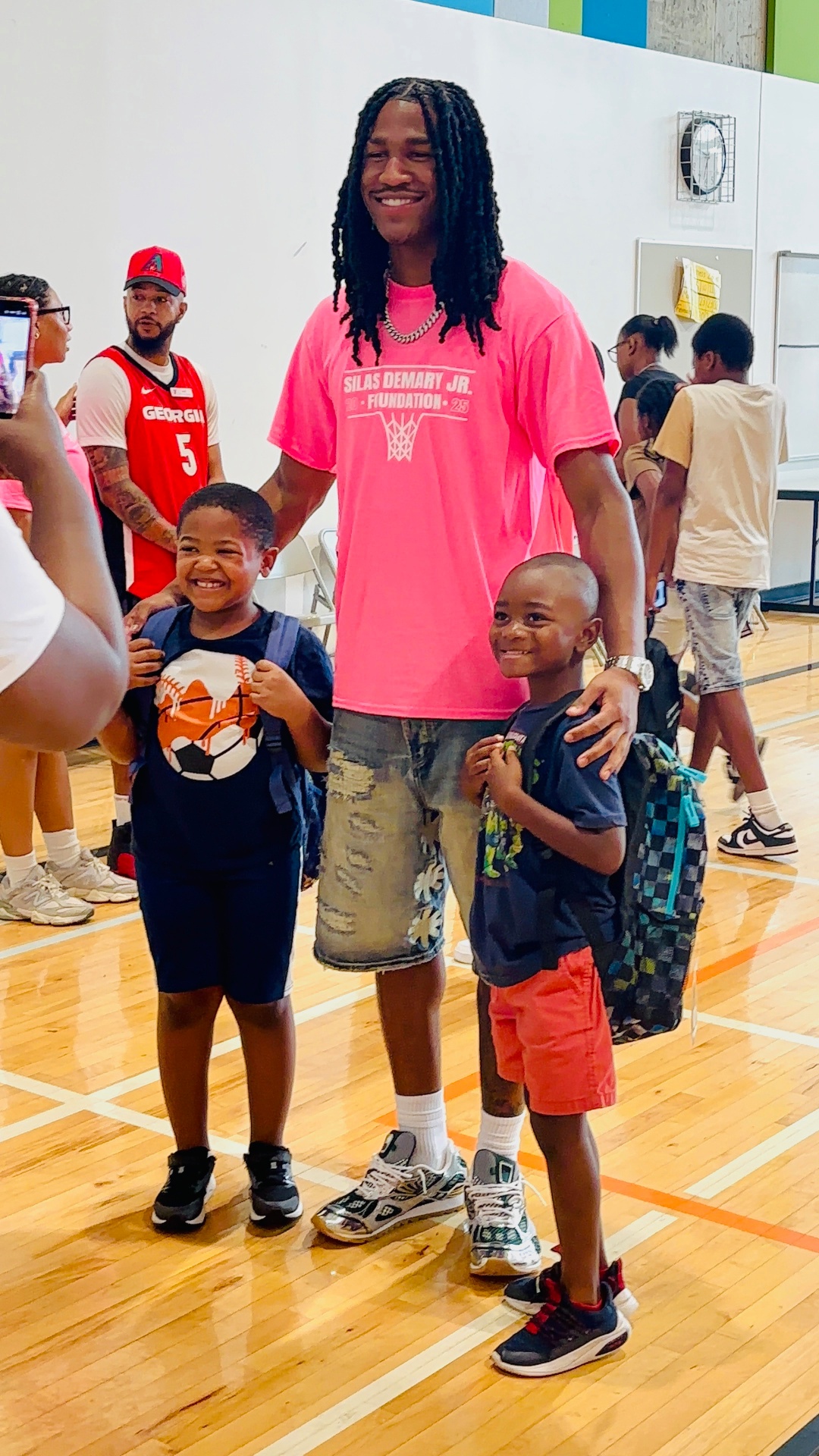 Silas Demary Jr. stands with two young boys holding their new backpacks at the 2025 Back to School Bash.