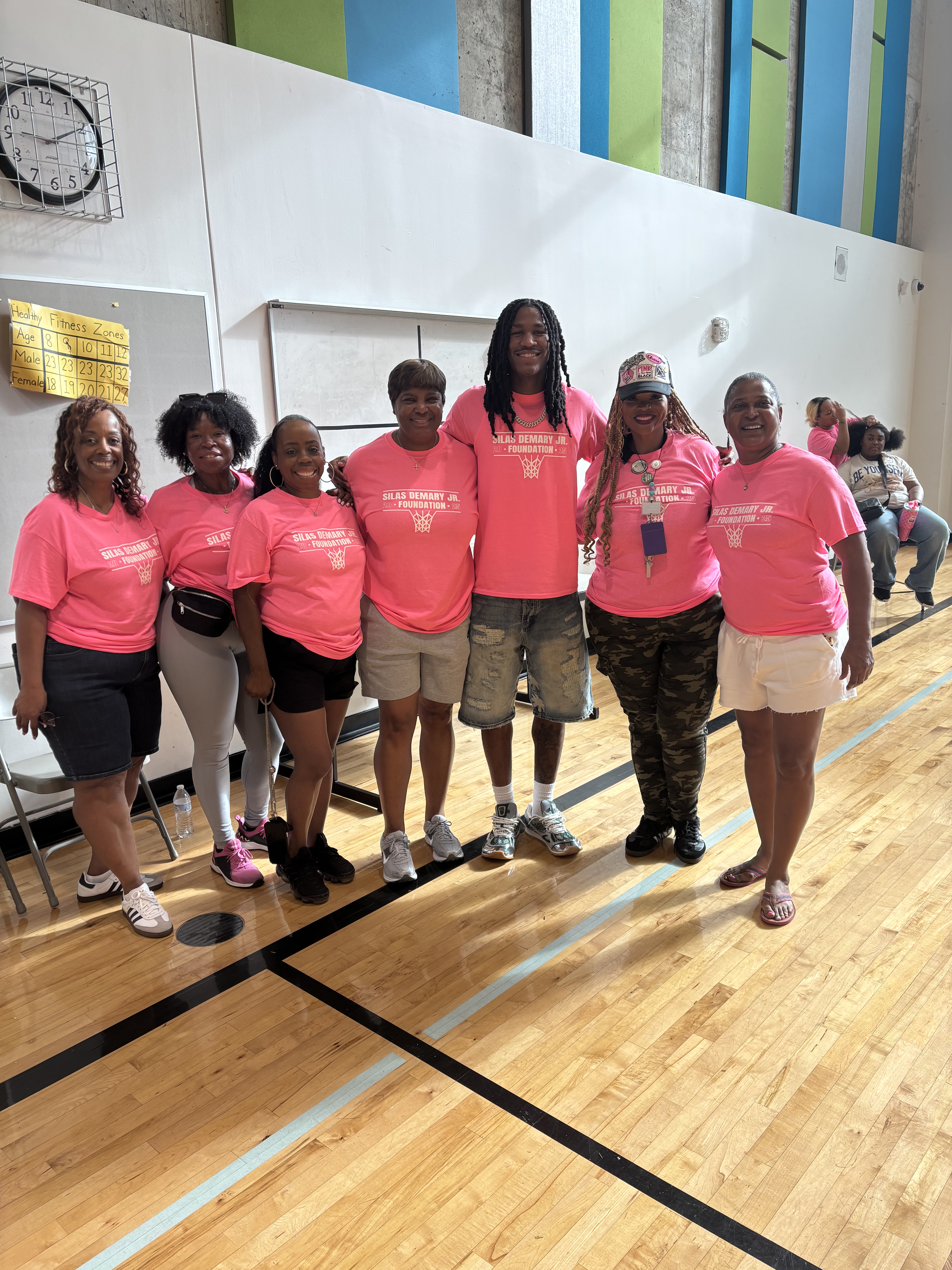 Silas Demary Jr. poses with foundation volunteers in matching pink shirts in the gym at the 2025 Back to School Bash.