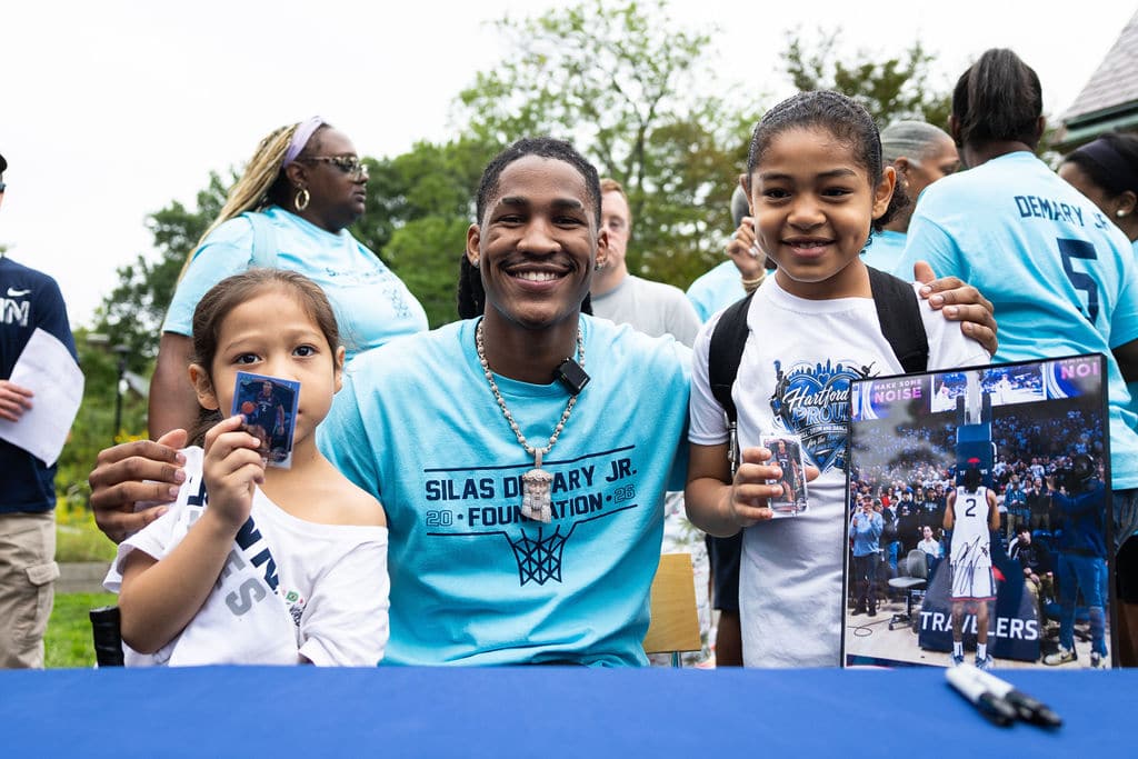 Silas Demary Jr. with two young fans holding signed photos and a poster