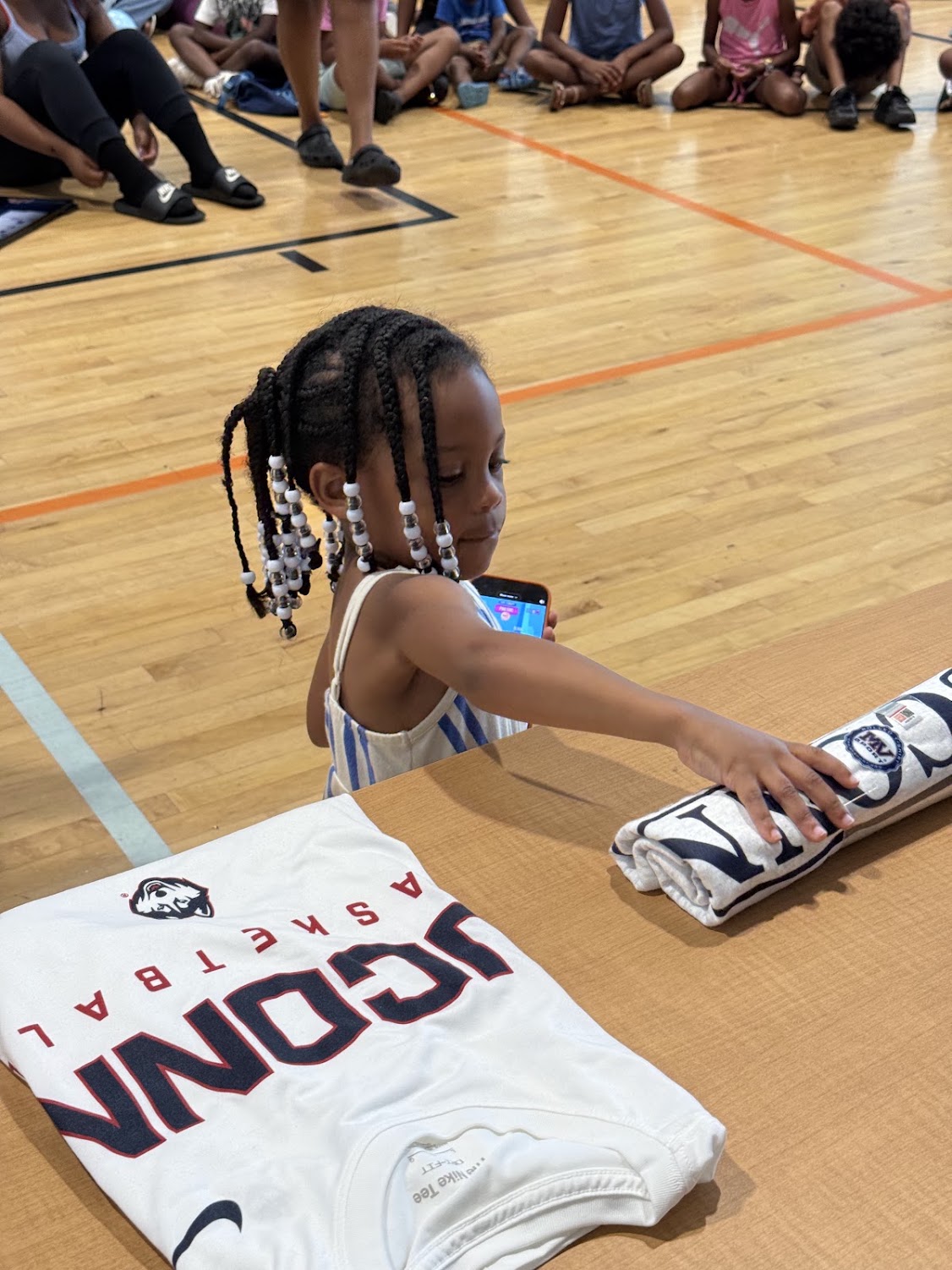 A young girl reaches for a rolled-up UConn towel on the gym floor at the Raleigh Back to School Bash.