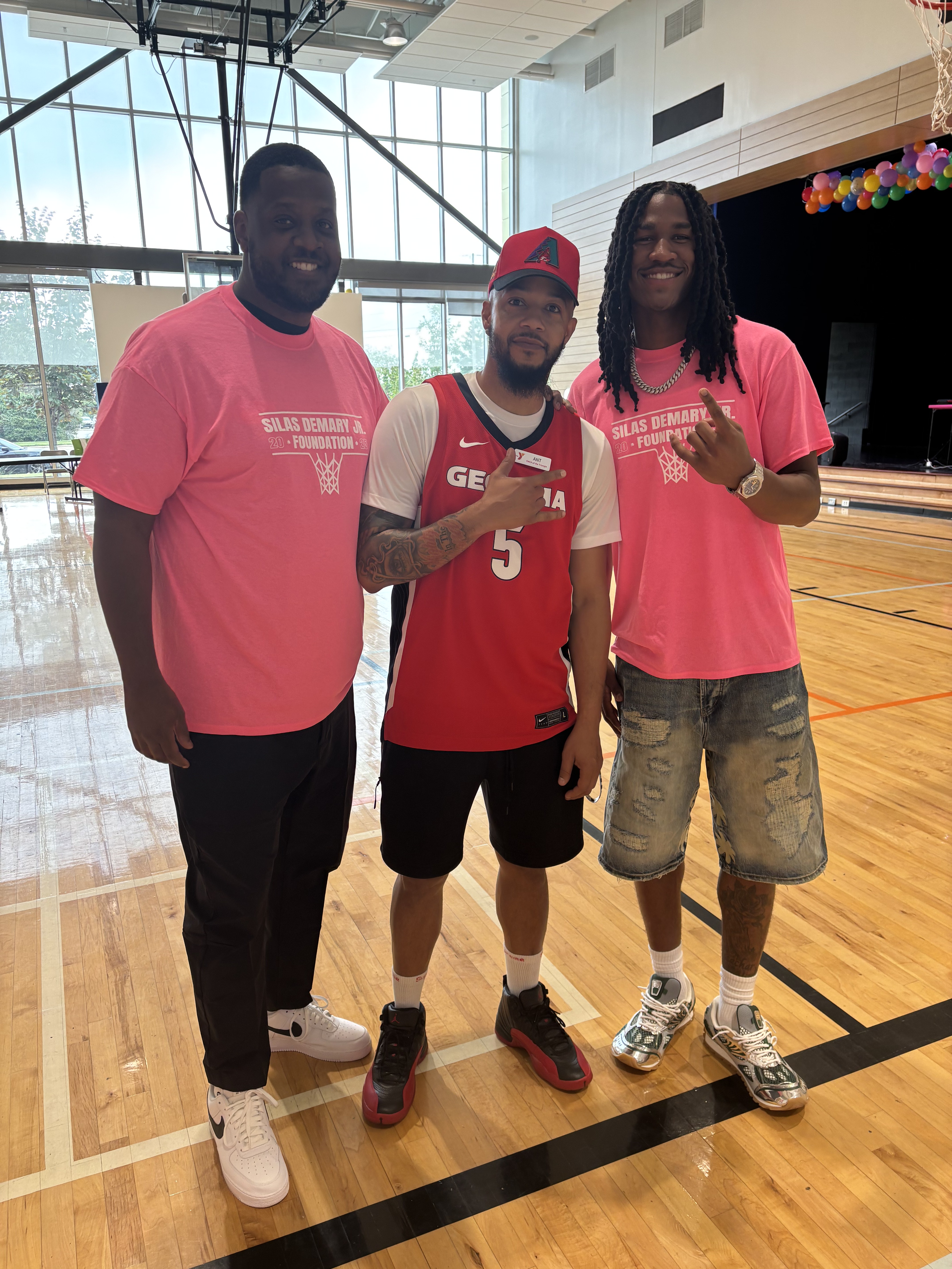 Silas Demary Jr. poses with two volunteers in the gym at the 2025 Back to School Bash.