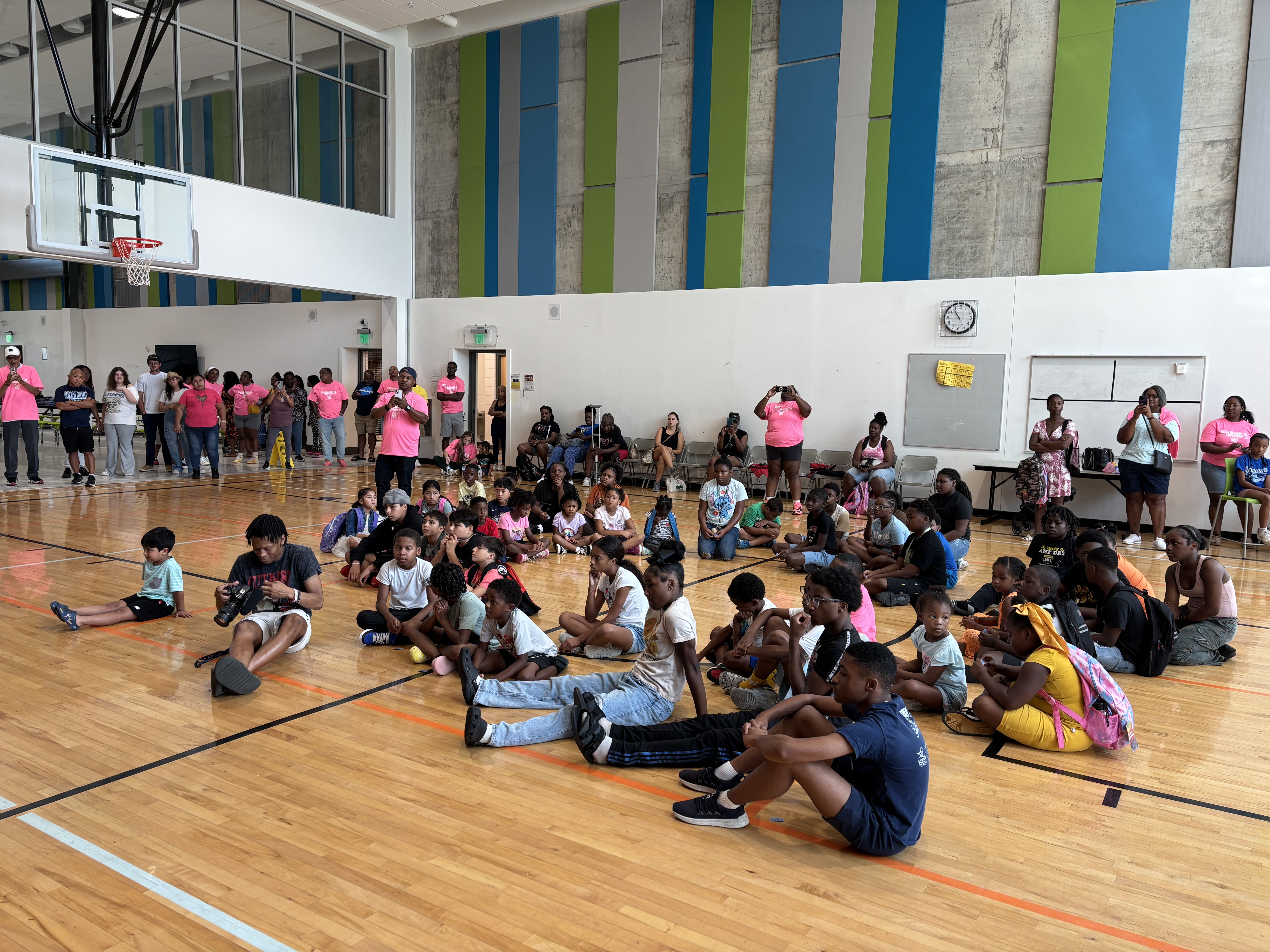 Students sit together on the gym floor as families and volunteers look on at the 2025 Back to School Bash.