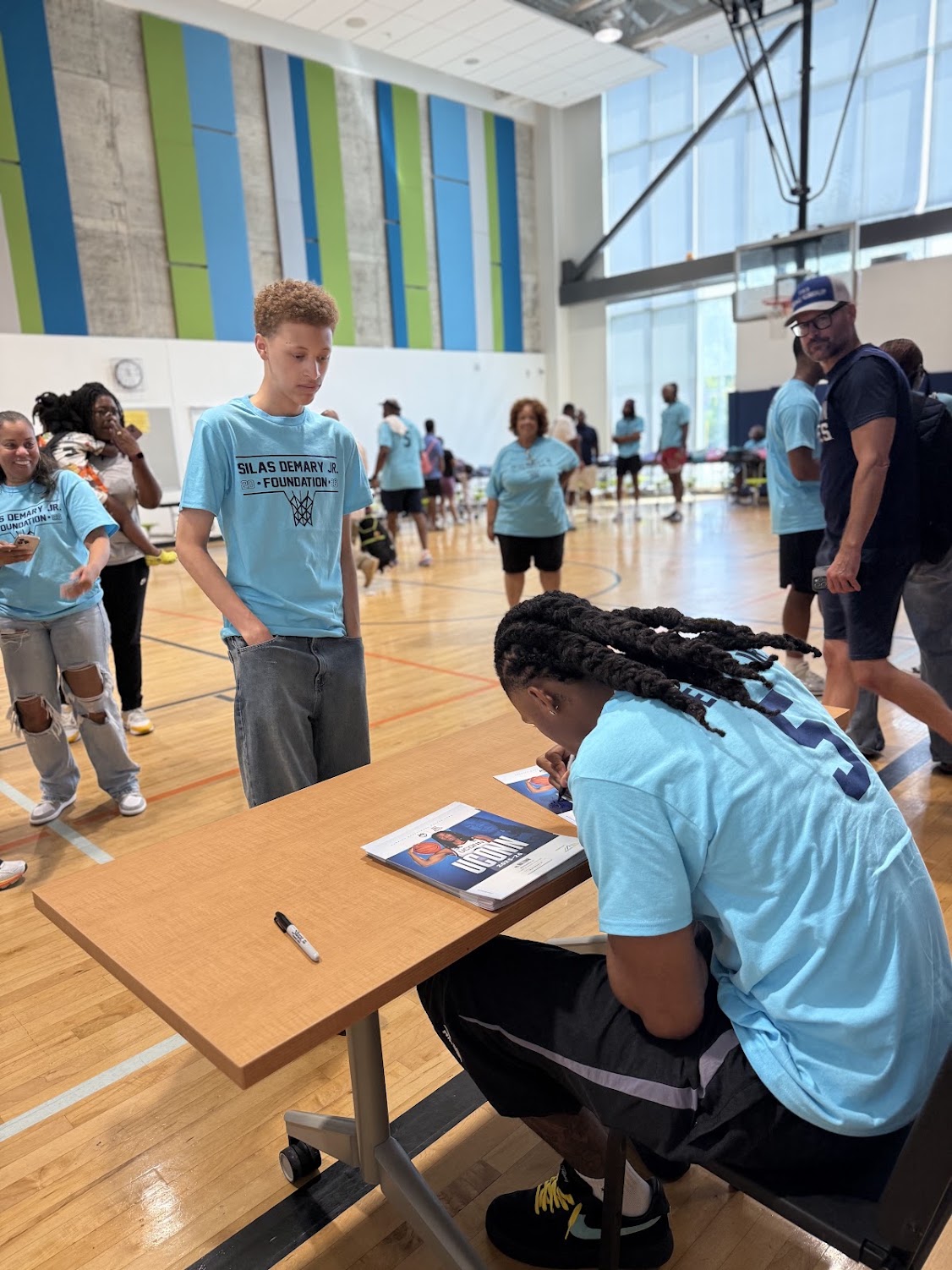 A teen in a foundation t-shirt watches Silas Demary Jr. sign an autograph at the Raleigh bash.