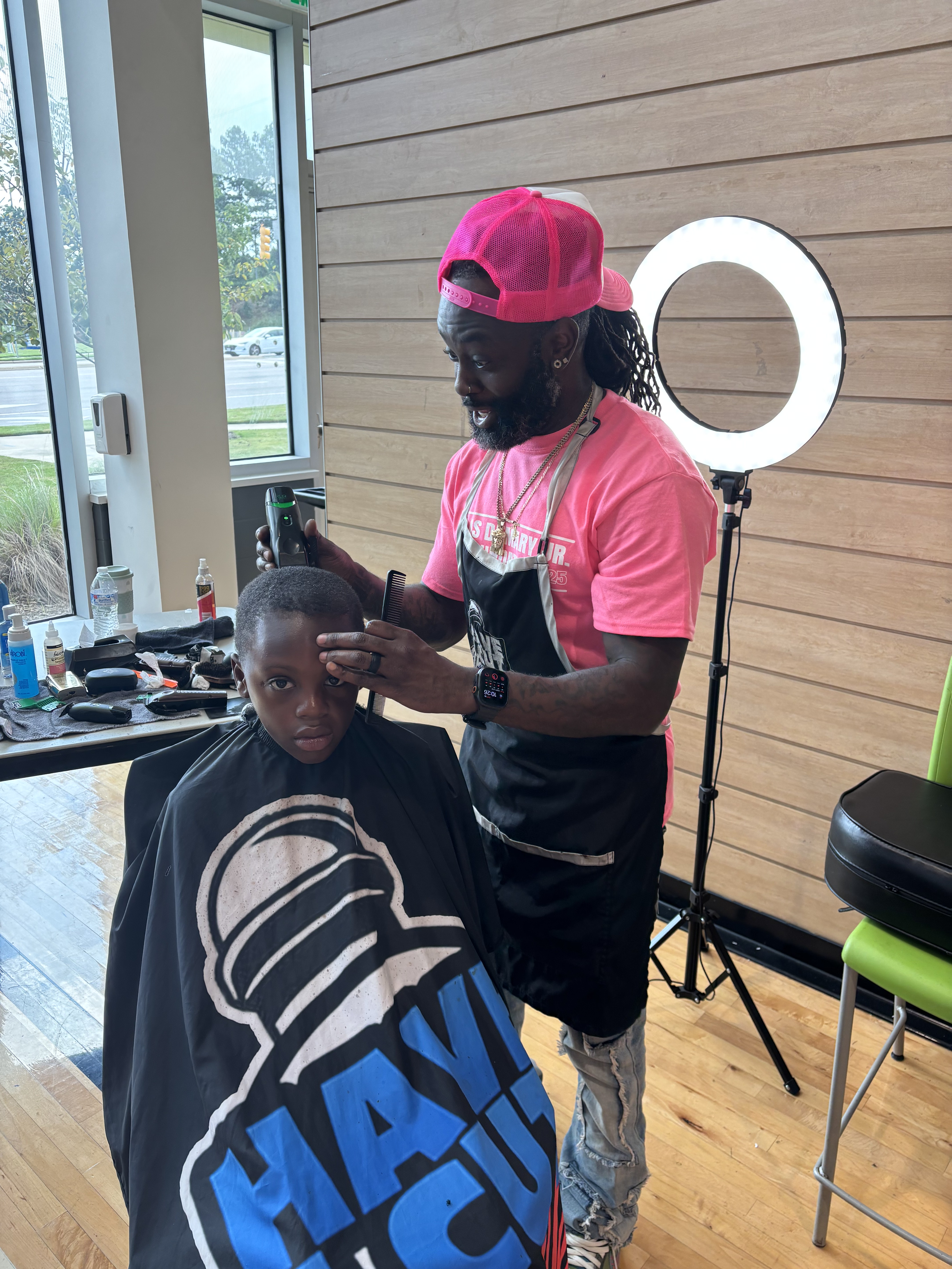 A barber in a pink foundation shirt lines up a young boy's haircut at the free barber station at the 2025 Back to School Bash.