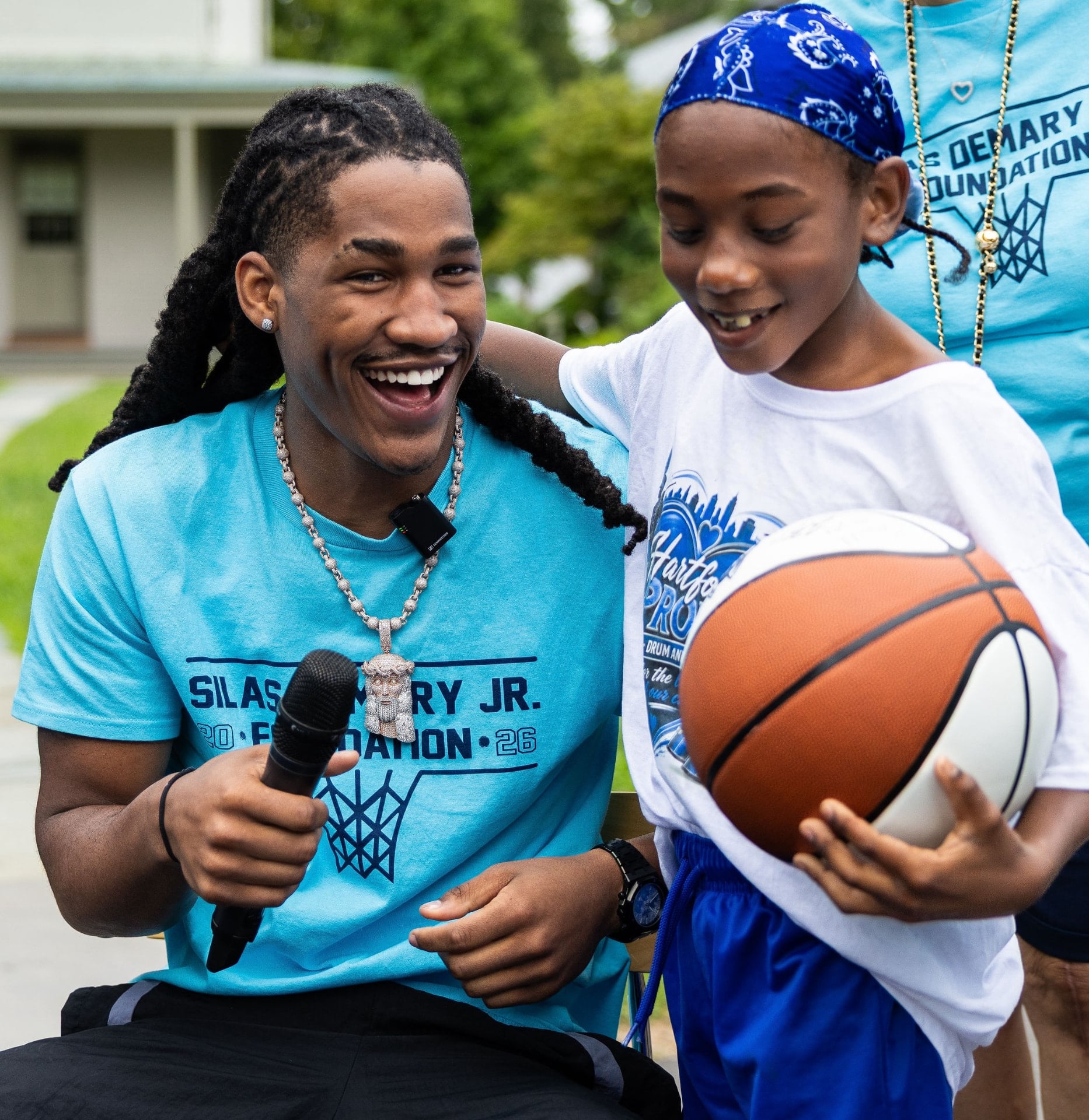 Silas Demary Jr. laughing with a young participant holding a basketball at a foundation event