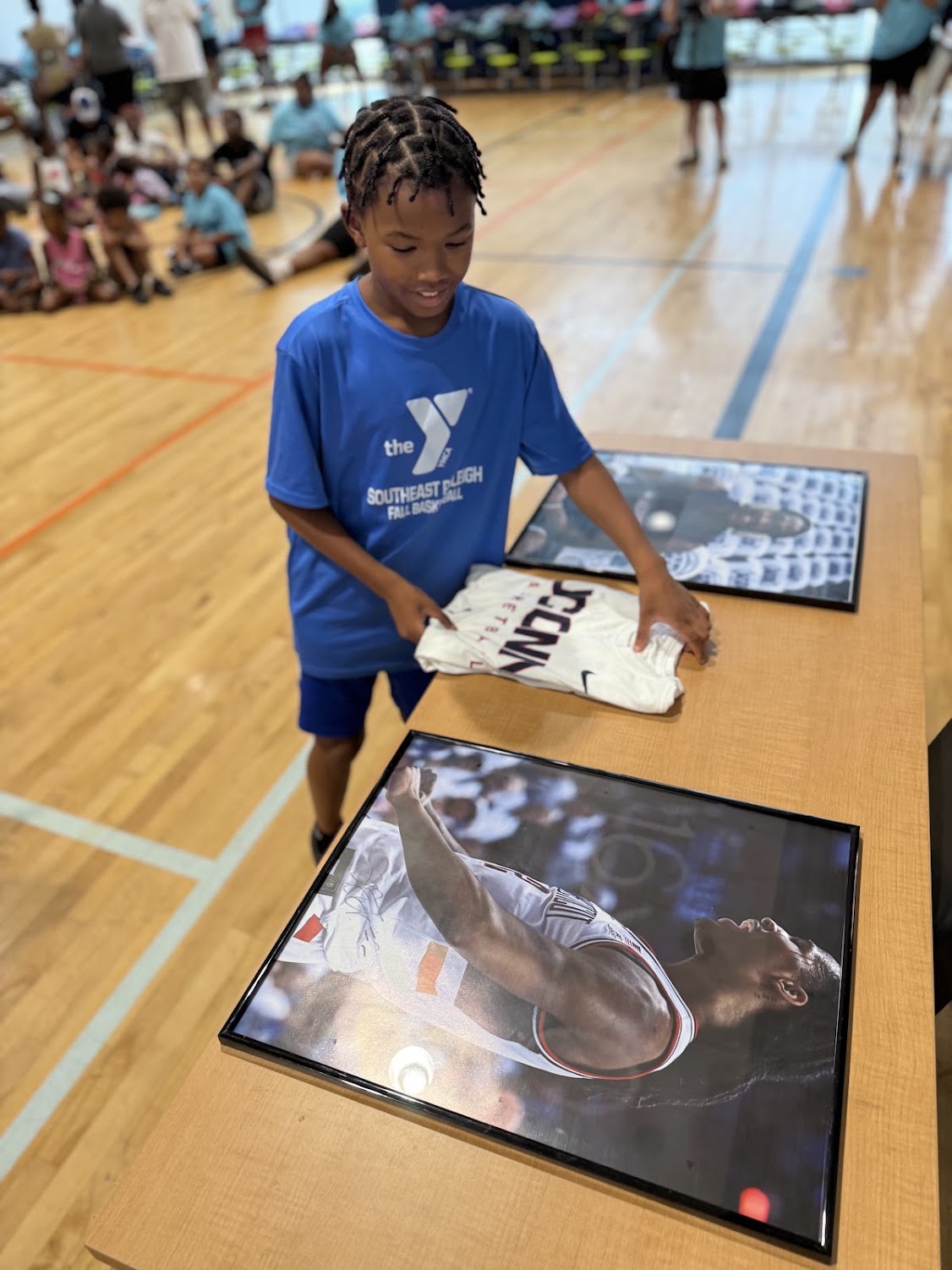 A young boy in a blue UConn shirt looks at framed memorabilia on the gym floor.