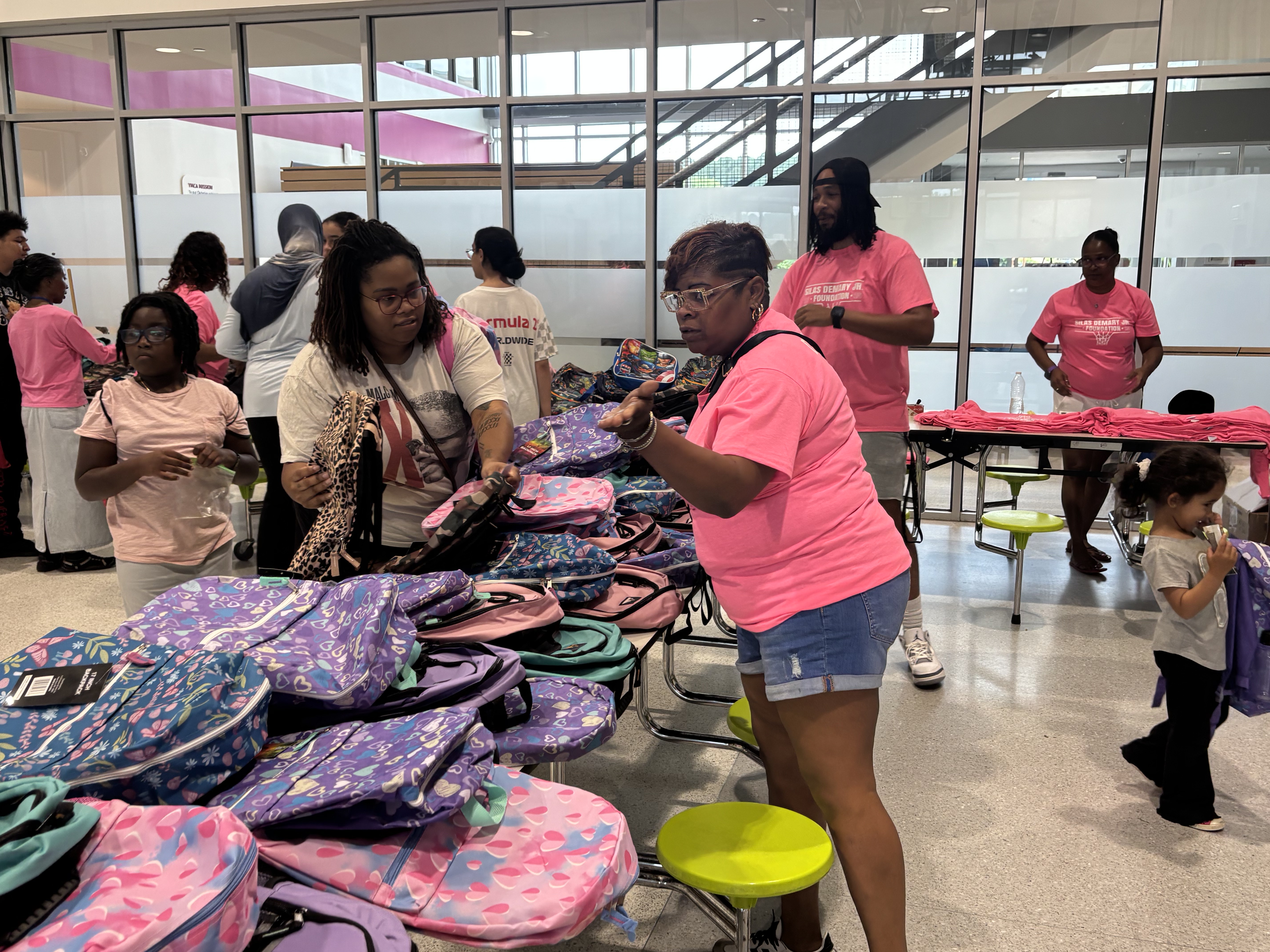 Volunteers in pink foundation shirts help parents choose backpacks at the 2025 Back to School Bash.